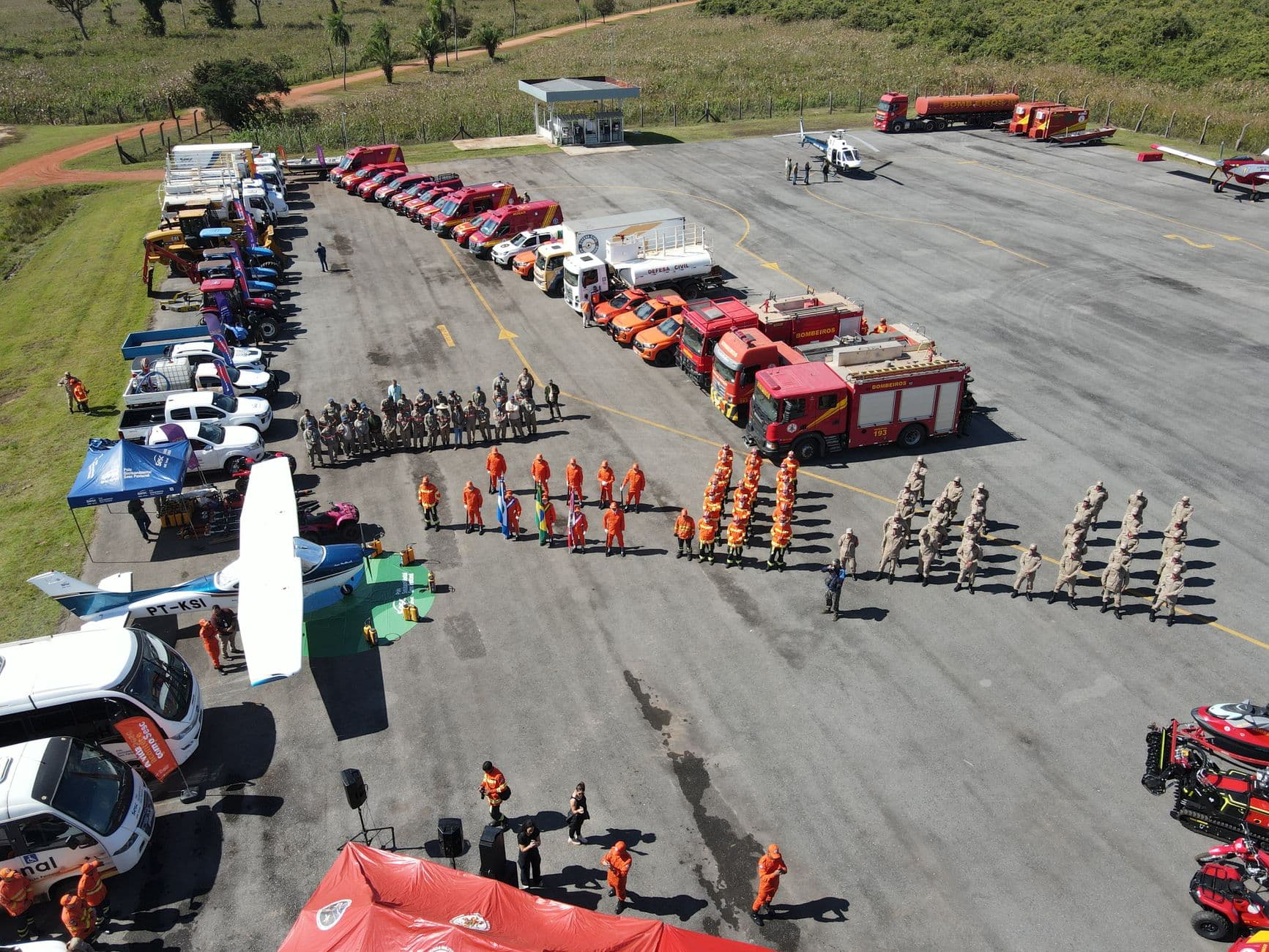 Aerial shot of fire trucks, emergency vehicles, and personnel in a training exercise. Clear day overview.