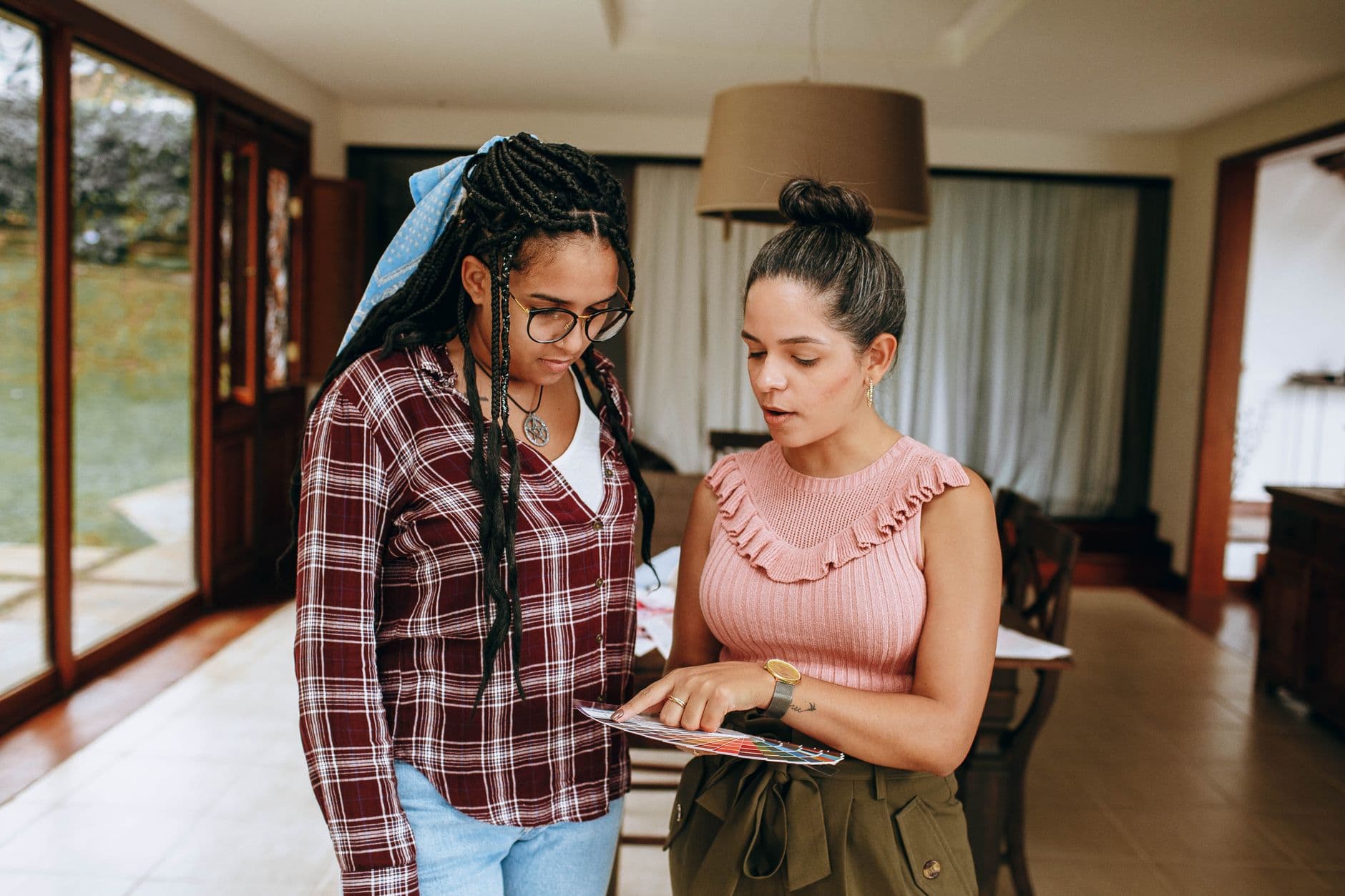Two women in casual clothing discussing a document in a bright indoor setting.